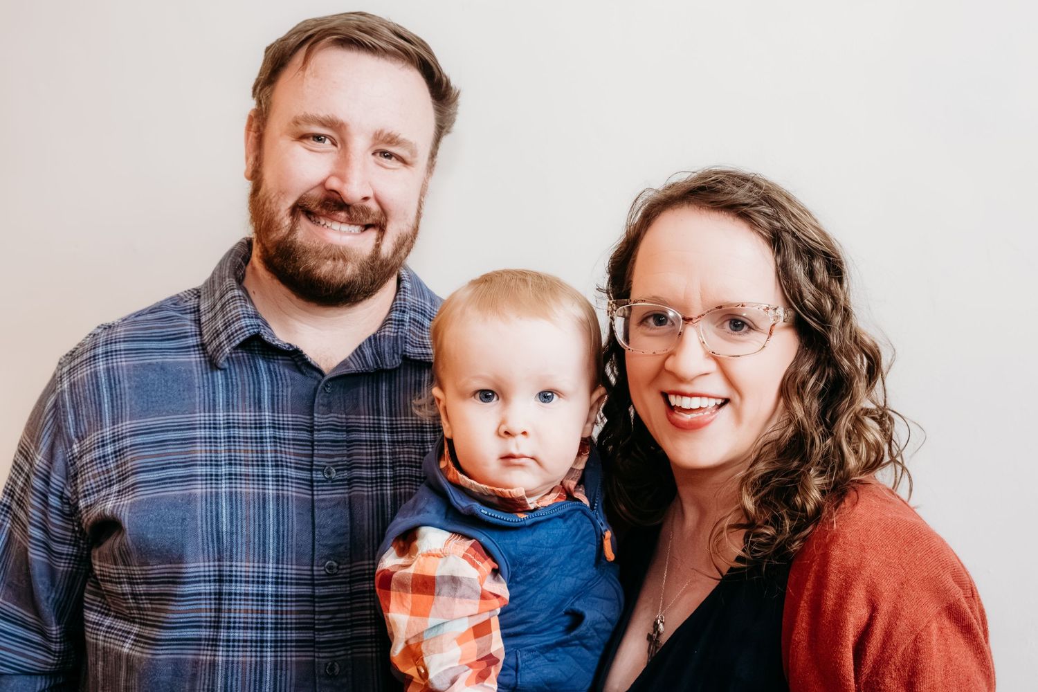 Studio portrait of father and mother standing closely together, holding their toddler son in between them.