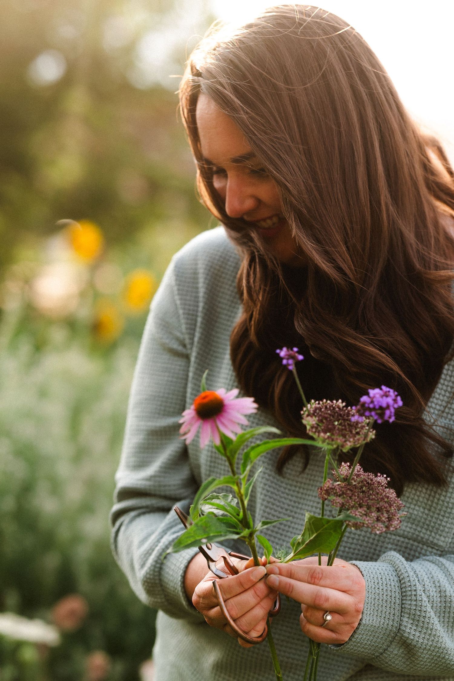 Portrait of Maggie of Maggie Theis Photography, holding several cut flowers, in her backyard garden.