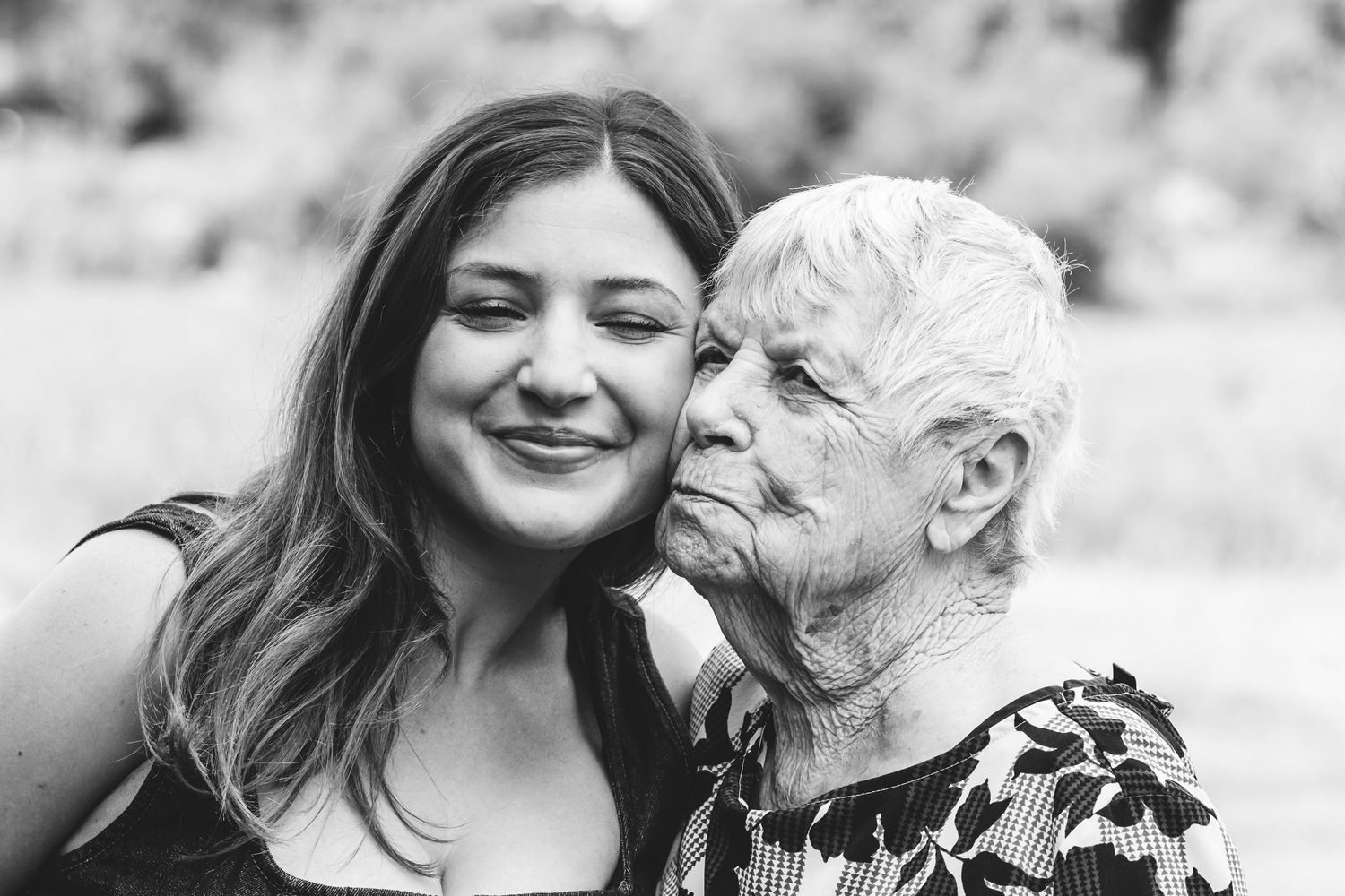 Black and white photo of adult grandchild cheek to cheek with grandmother.