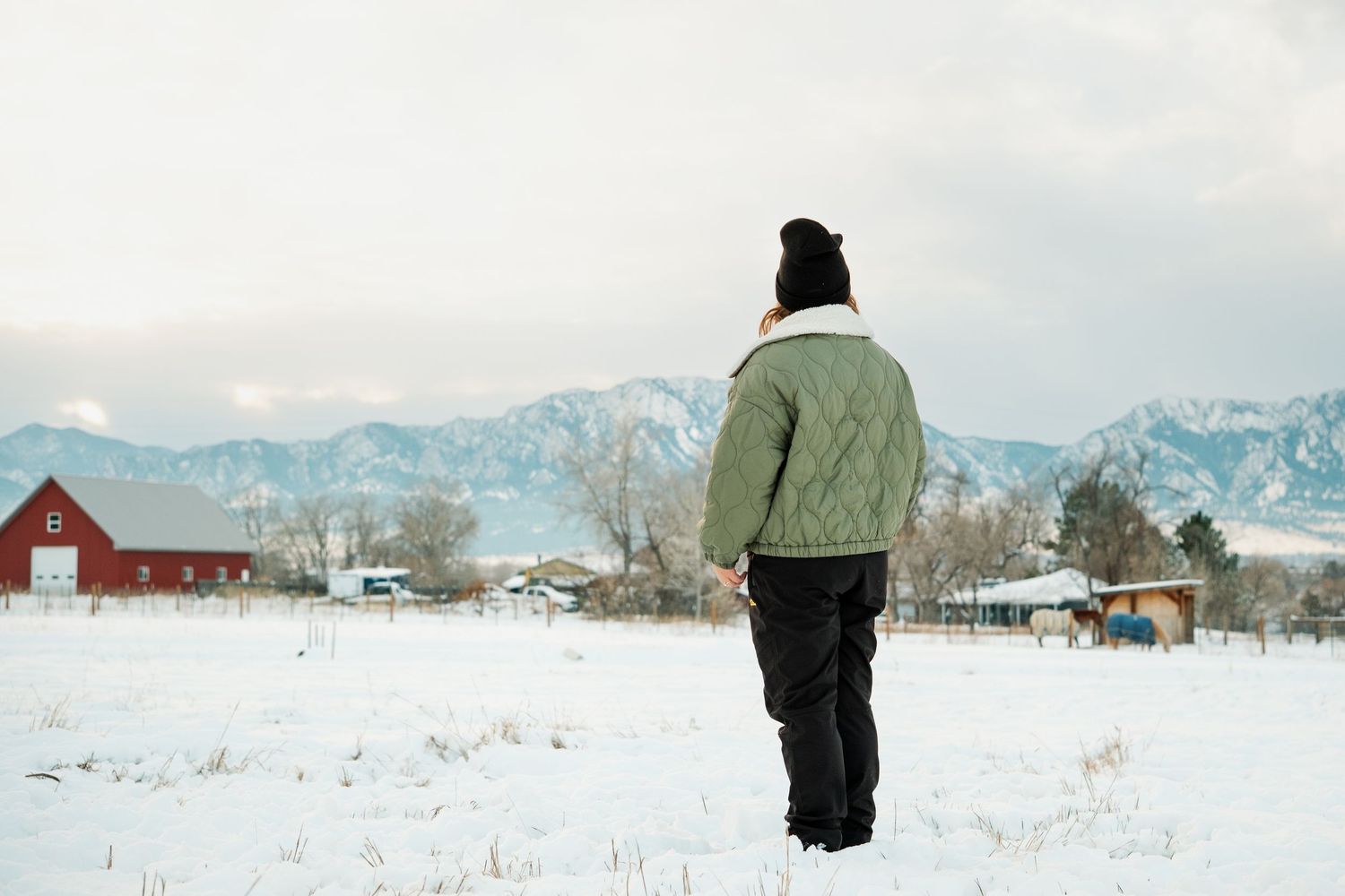 Mother standing in snow, looking away from camera, toward Boulder flat irons on a snowy day.