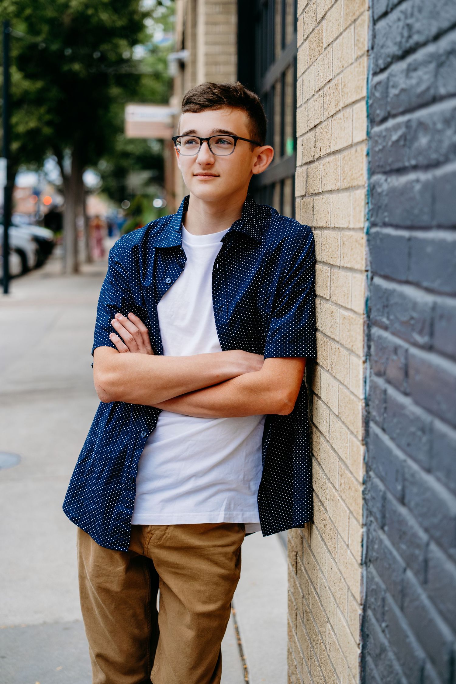 Senior portrait of a teenage boy in downtown Fort Collins, leaning casually against a brick wall. Captured by a Denver senior photographer,