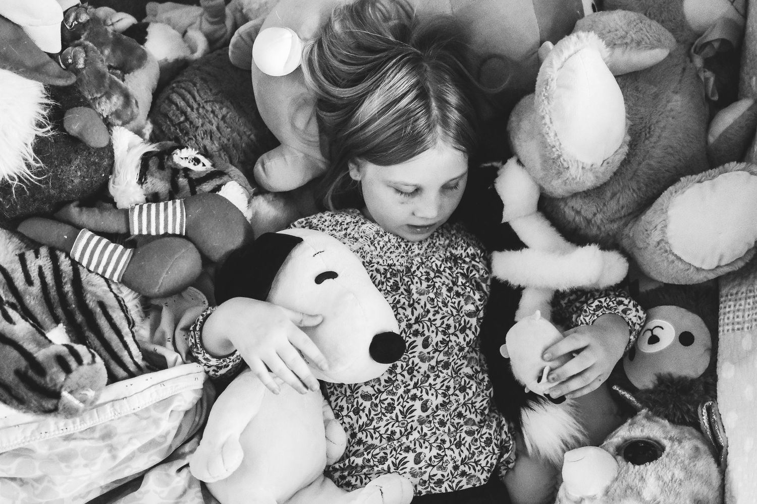 Overhead view of girl laying amongst a pile of stuffed animals.