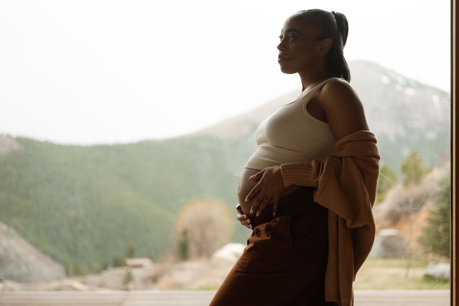 Silhouette of pregnant mom, backlit by cloudy skies and Boulder foothills.