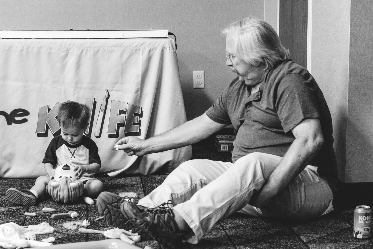 Black and white of grandfather sitting on floor playing with grandson.