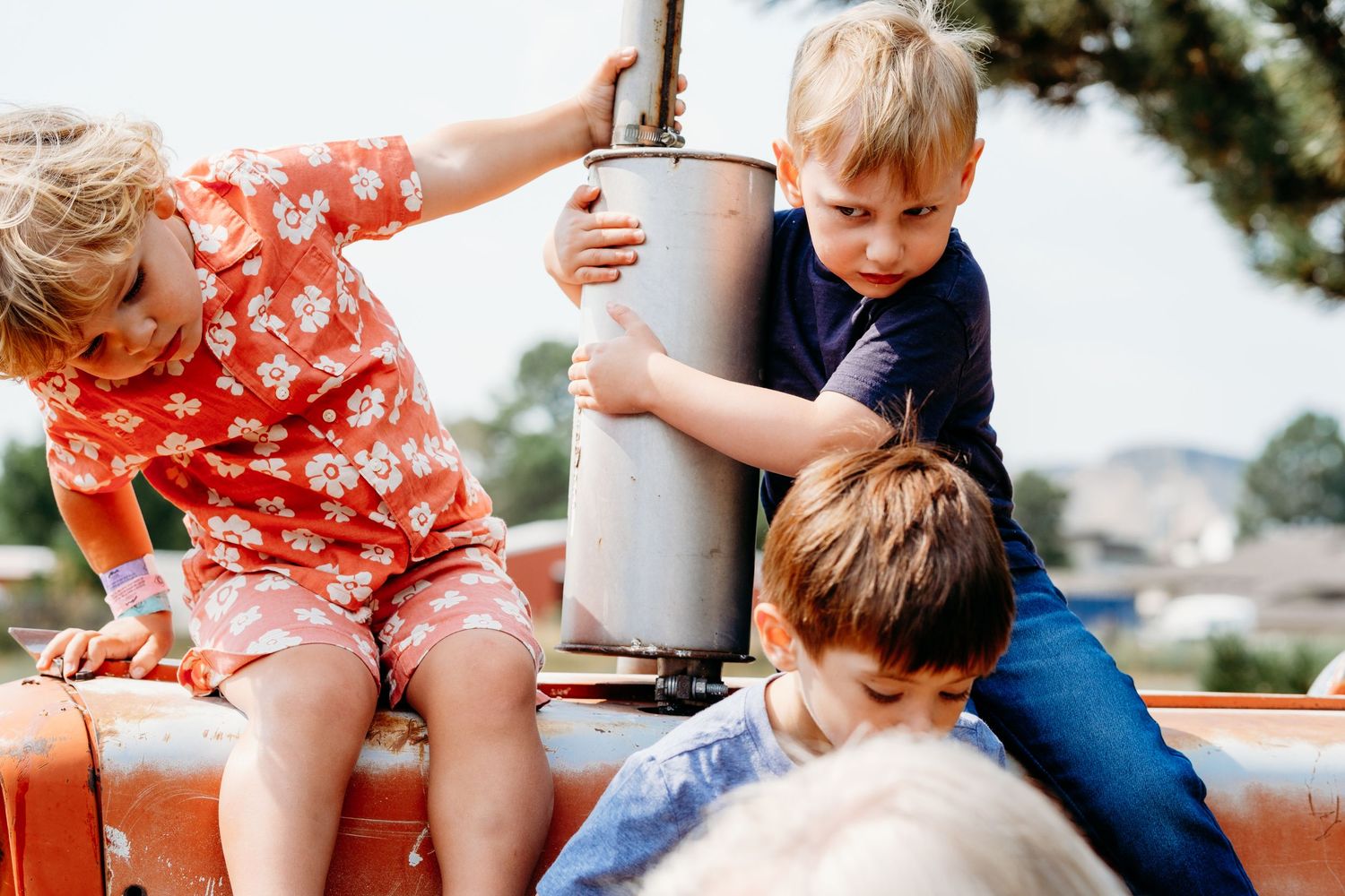 Silly portrait of young boys sitting on tractor, one boy holding on tightly.