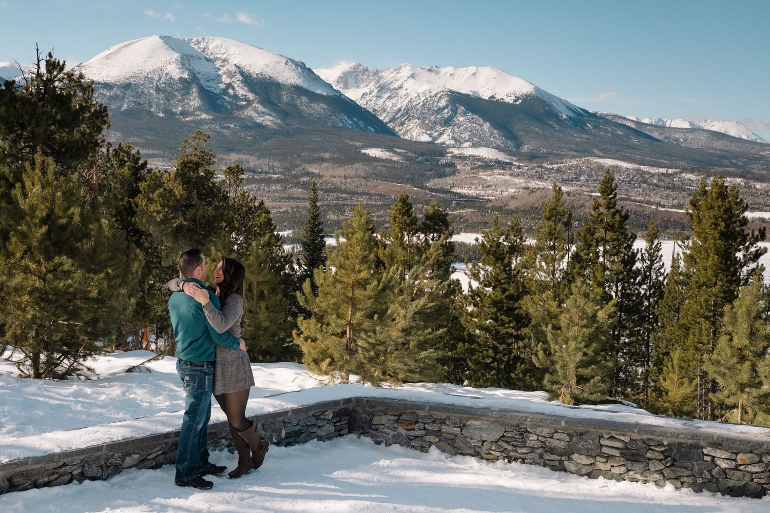 Couple standing together, embracing, at amphitheatre at Sapphire Point Overlook, snowcapped mountains in the background.