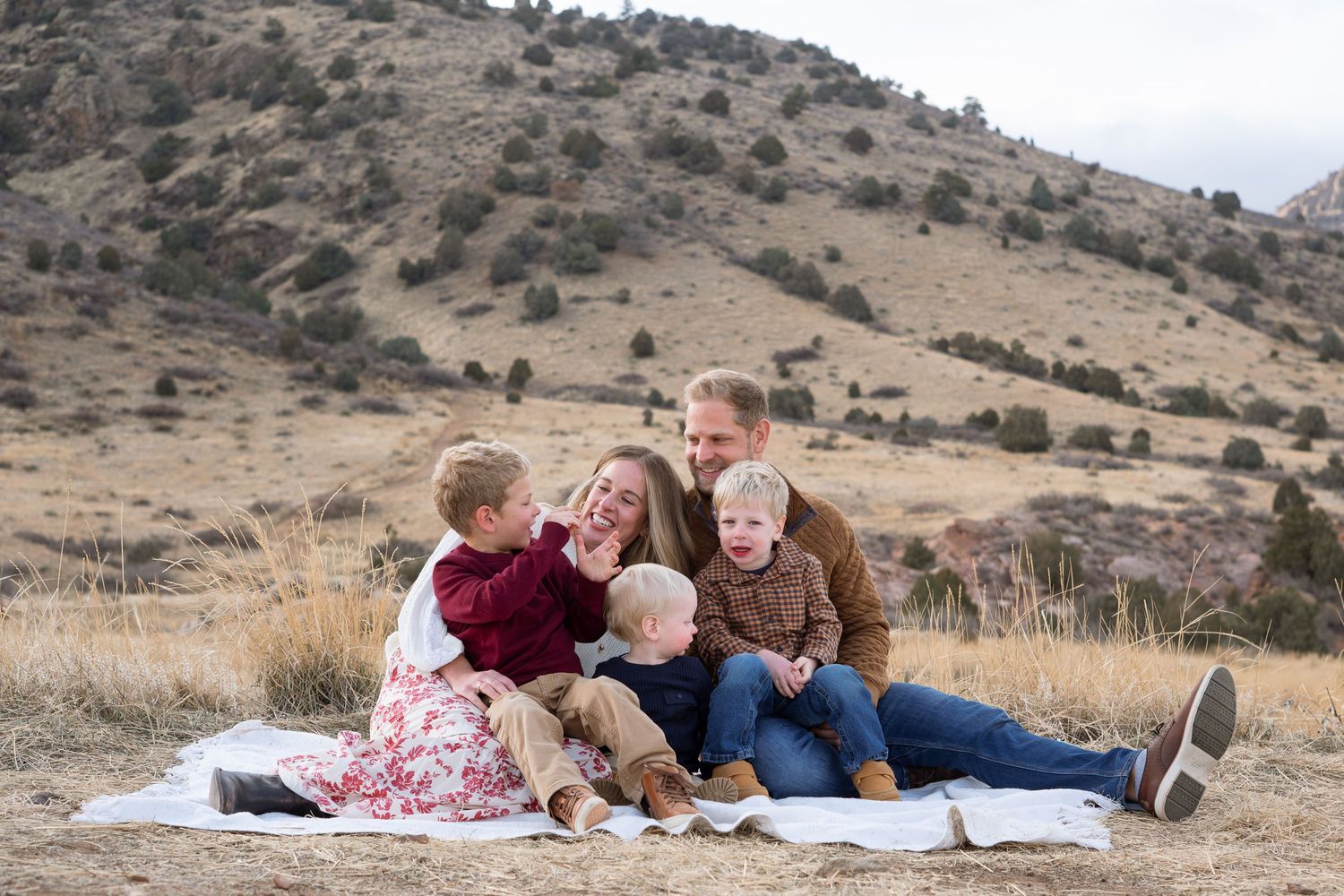Family of five sitting on white blanket, all snuggled together.