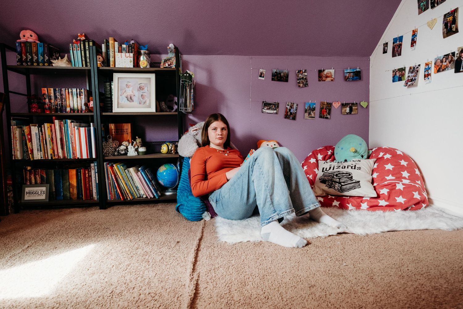 Serious portrait of teen girl sitting in her room, surrounded by books and photographs.