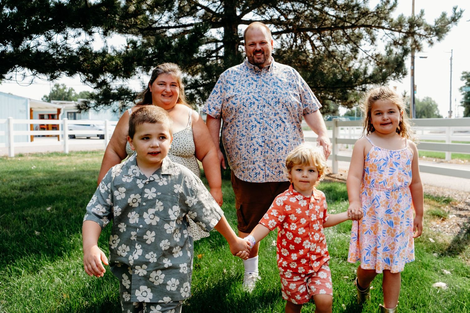 Playful walking portrait of three children holding hands and parents walking behind them on family property.