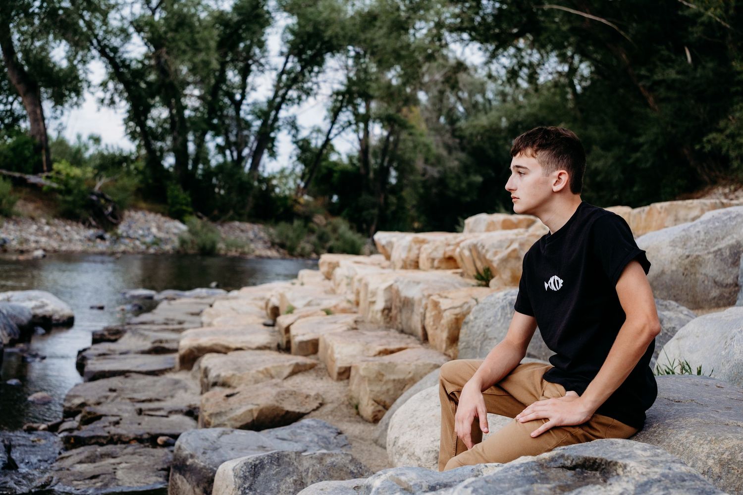 Serious portrait of profile of teen boy sitting on rock wall steps, gazing out toward the Cache la Poudre.