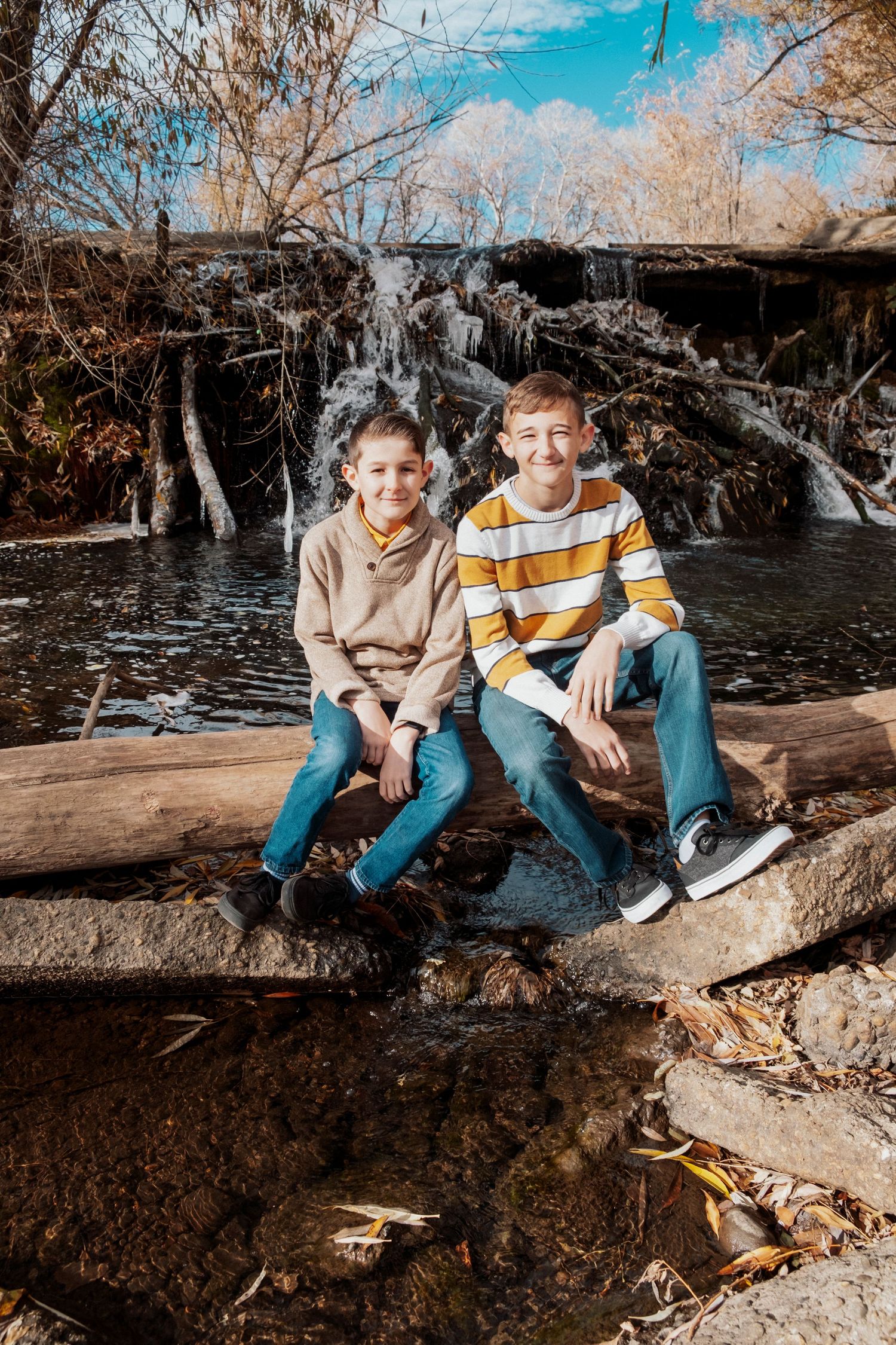 Two brothers sitting in front of waterfall at Golden Ponds Park in Longmont, Colorado.