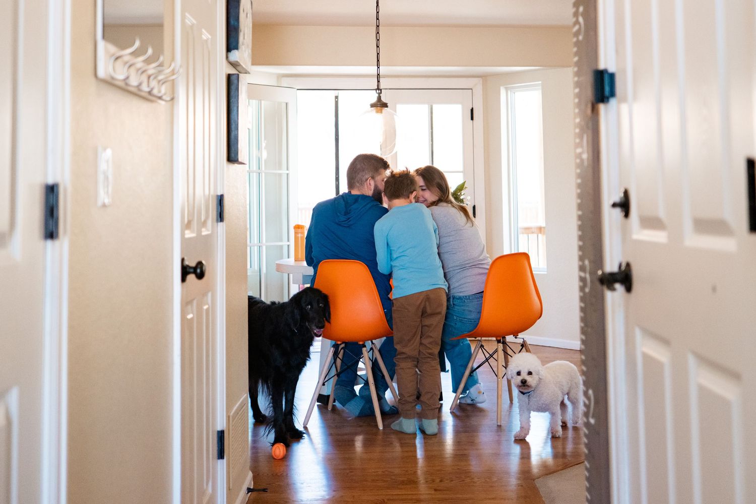 Parents sitting at kitchen table, son peeking over their shoulder, two dogs looking into the camera.