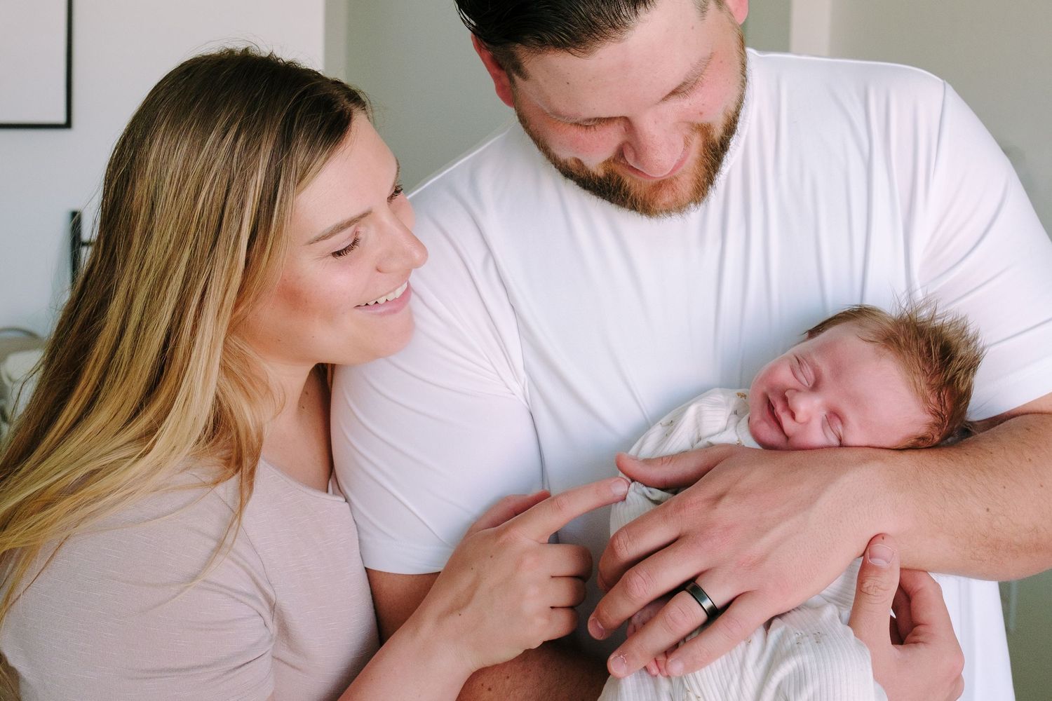 Sentimental newborn portrait in home session ,father holding newborn, mother snuggling close to father, newborn has a sleepy smile.