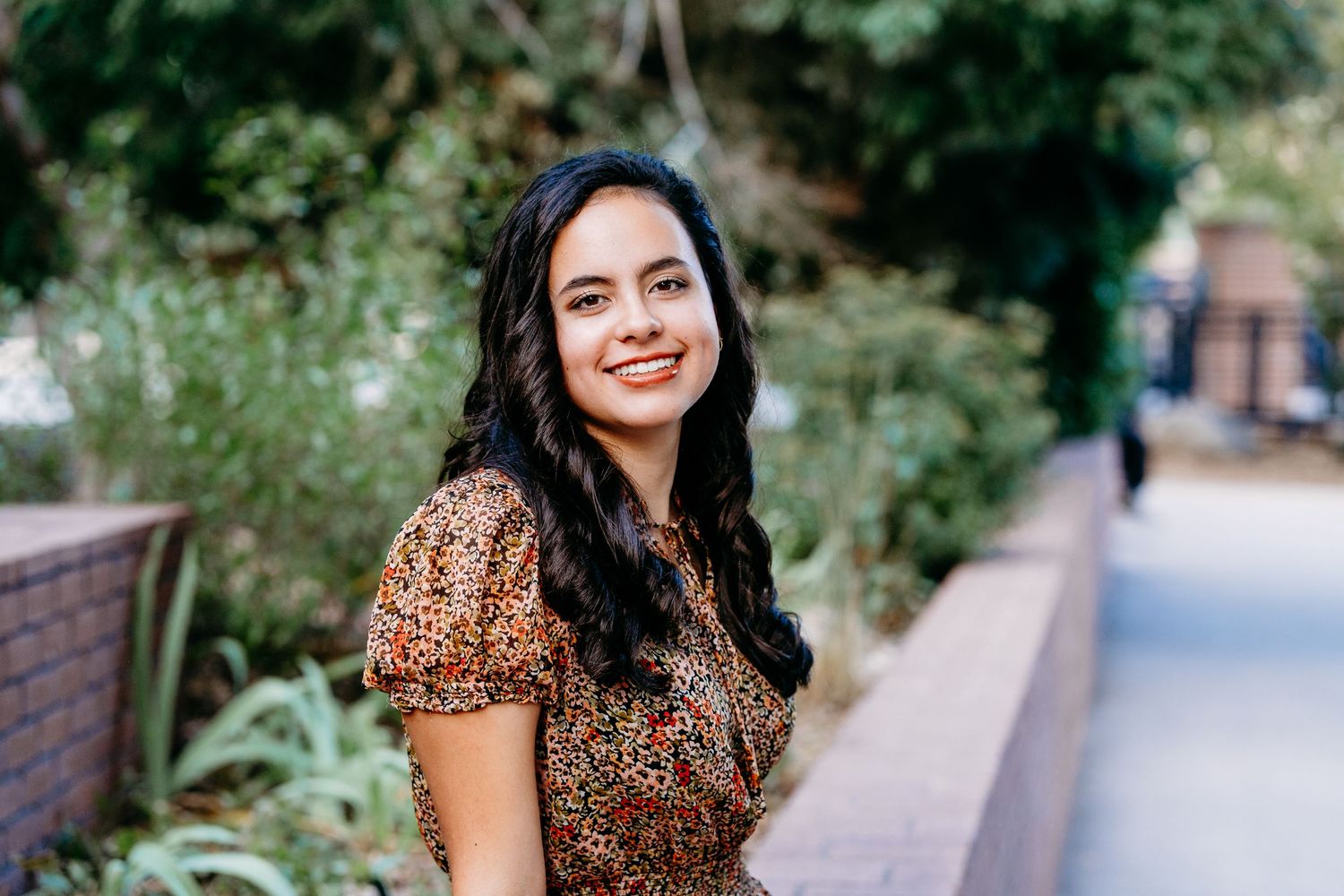 Senior portrait of smiling teen female with greenery and cement walking path in background.
