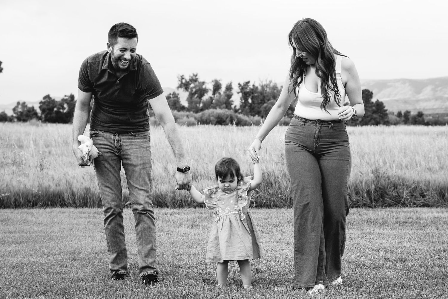 Man and woman walking in park, each holding hands of toddler girl who walks between them, in park in Arvada, Colorado.