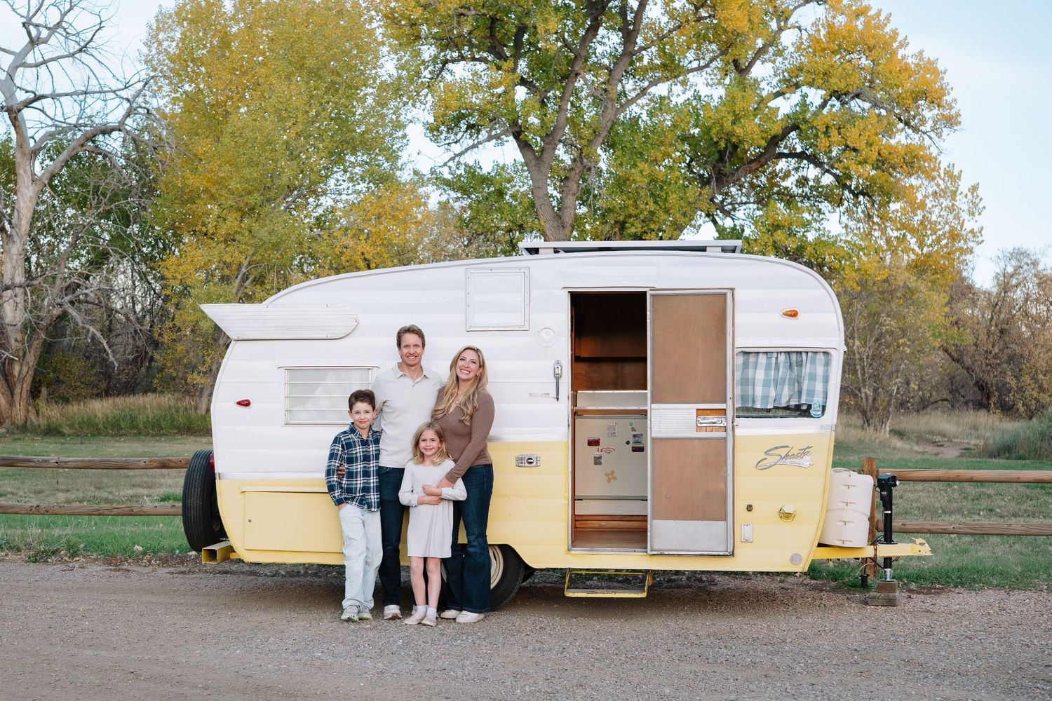 Family of mother, father and two children in front of vintage, yellow Shasta trailer at Bear Creek Lake Park in Lakewood, Colorado.