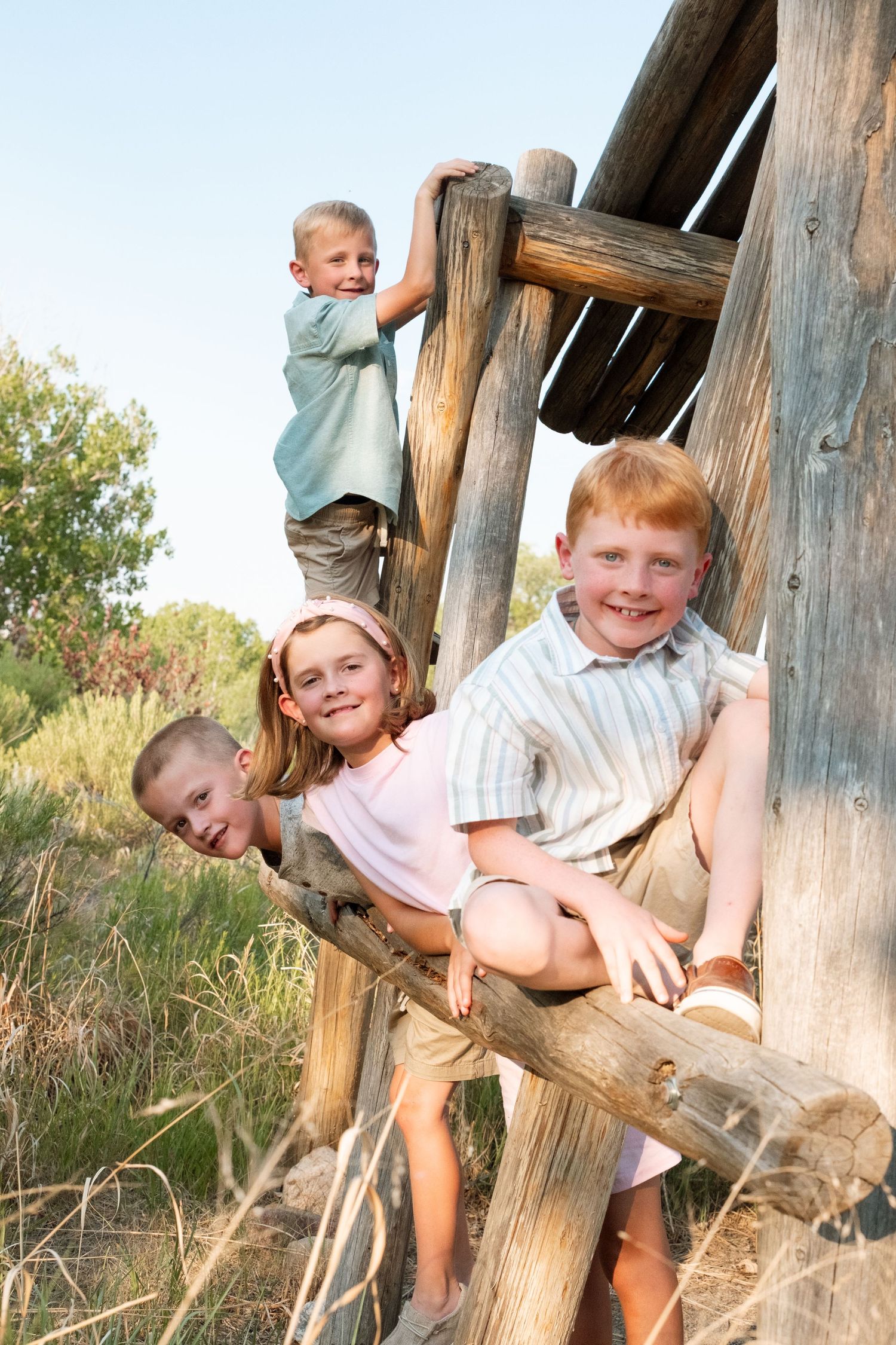 Portrait of four cousins perched on a wooden structure, all smiling on a summer day at a Denver park.