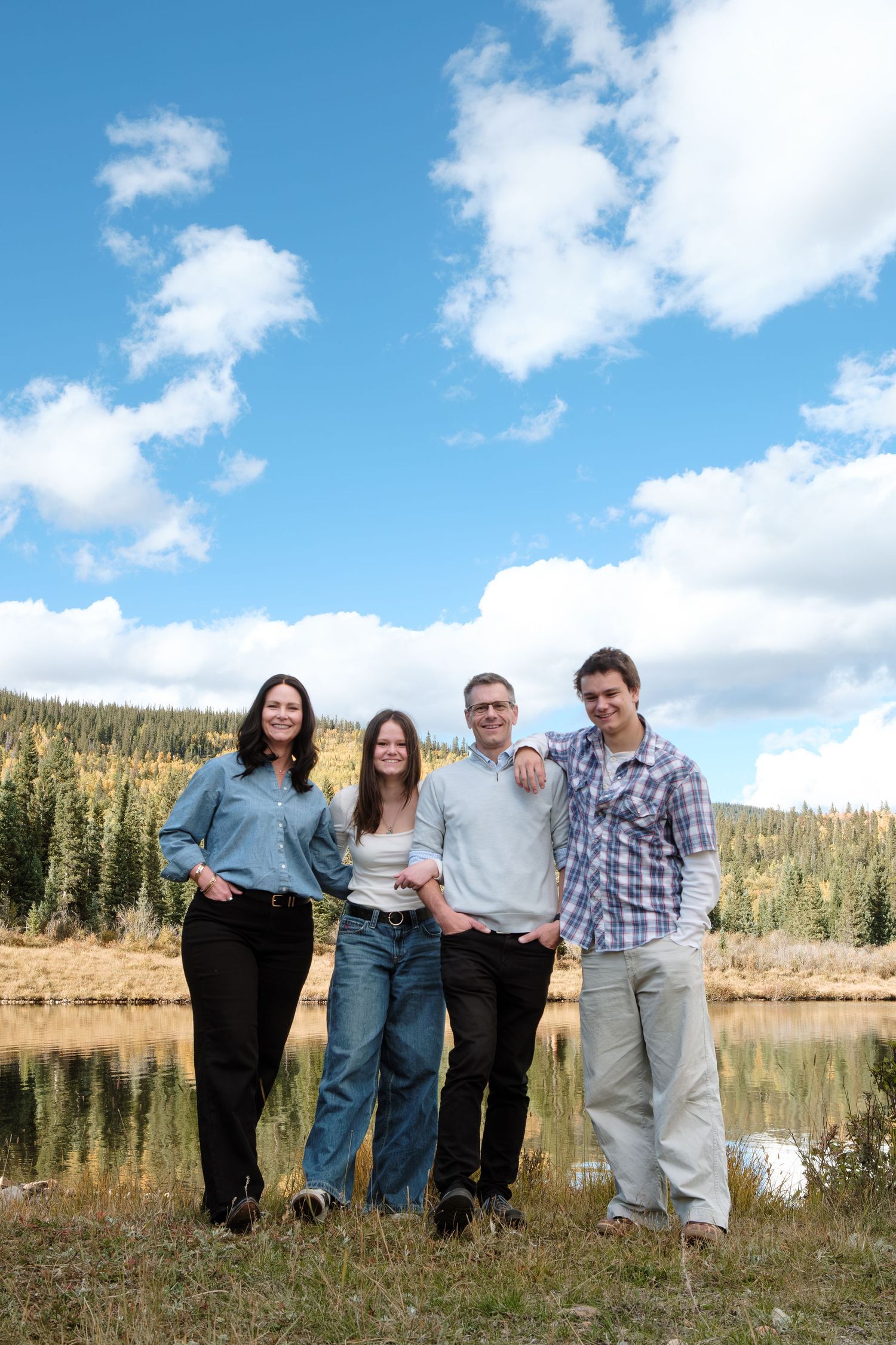 Family of four standing in front of blue skies in Colorado mountains.