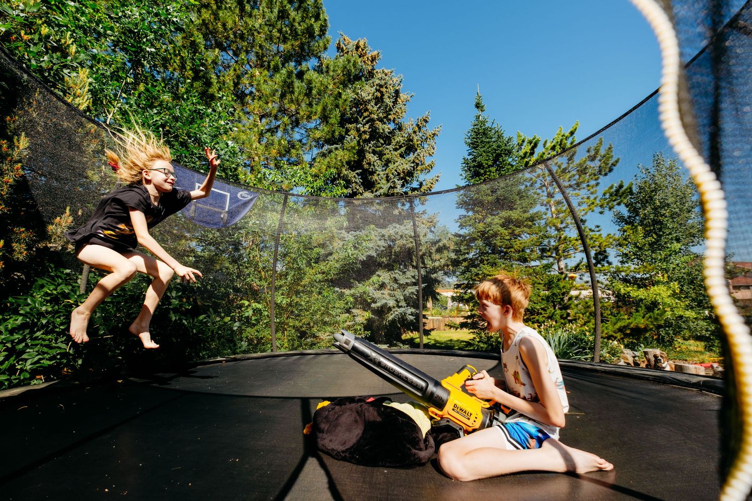 Denver photographer's project 365, June, children playing on trampoline, one pointing a leaf blower at the other, her hair blowing wildly.