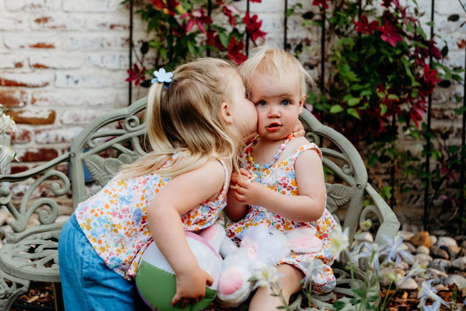 Toddler sister kissing her sister on the cheek.