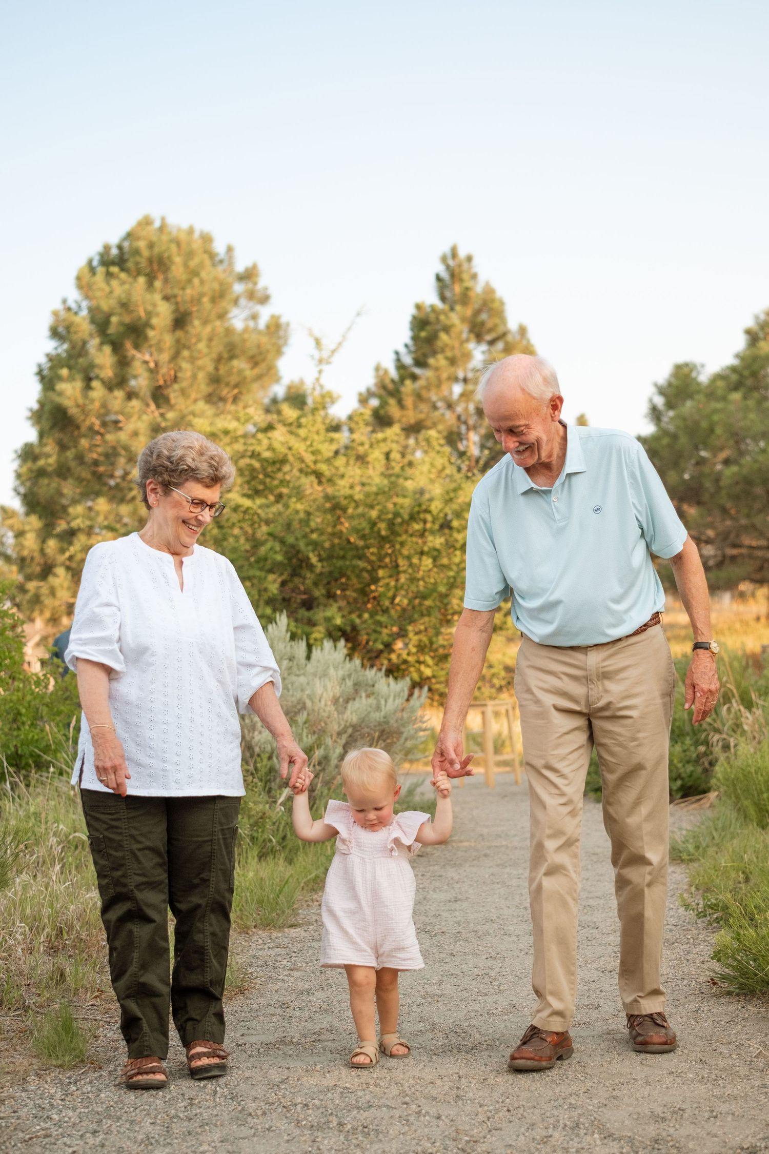 Grandmother and grandfather walking on each side of granddaughter, each holding one of her hands, gazing toward her.
