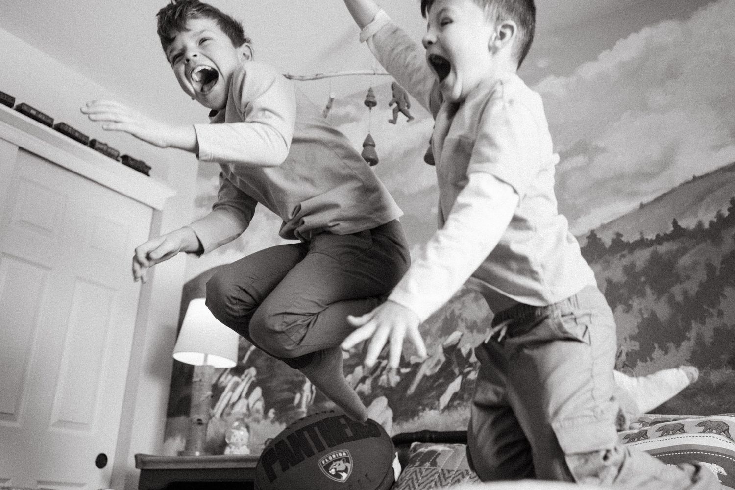 Black and white portrait of boys jumping on bed, both laughing mid air.