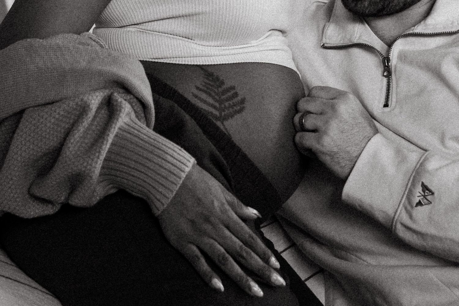 Black and white portrait of pregnant mother with fern tattoo on belly, father lovingly placing hand on belly.