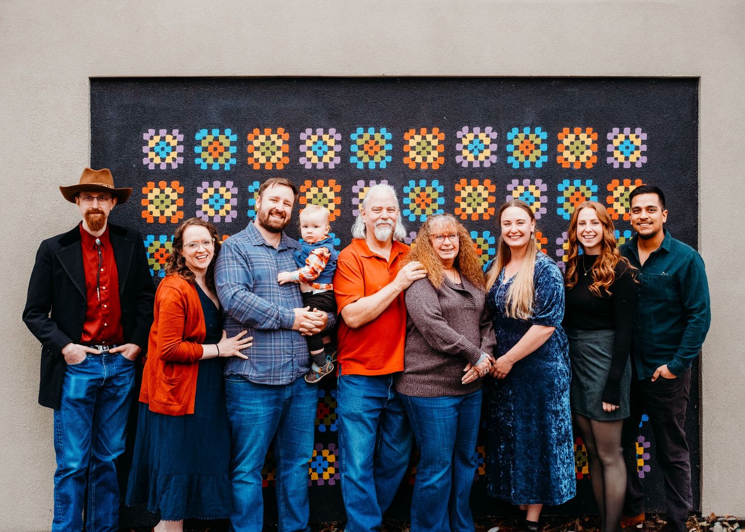 Extended family portrait of two grandparents, three children and two spouses and one grandchild, in front of colorful mural in Denver, CO.