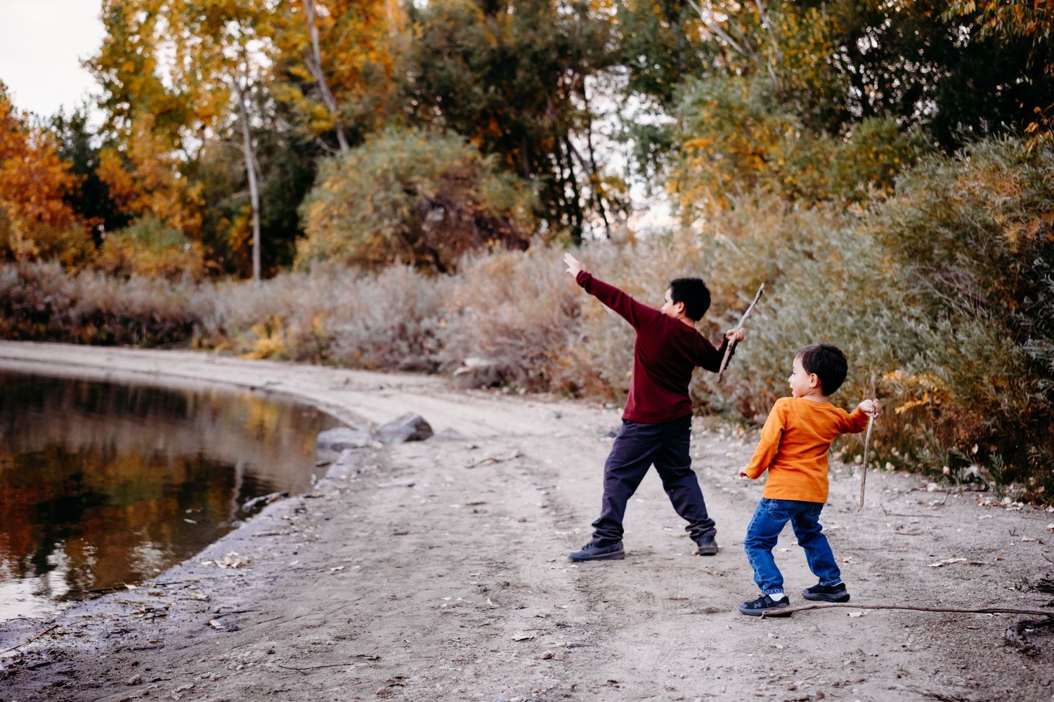 Brothers playfully throwing sticks into water at Bear Creek Lake Park in the city of Lakewood.