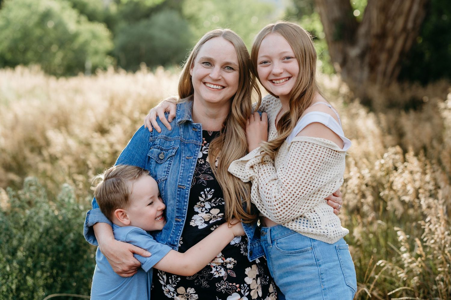Mother standing, son hugging mom, daughter snuggling mom on other side.