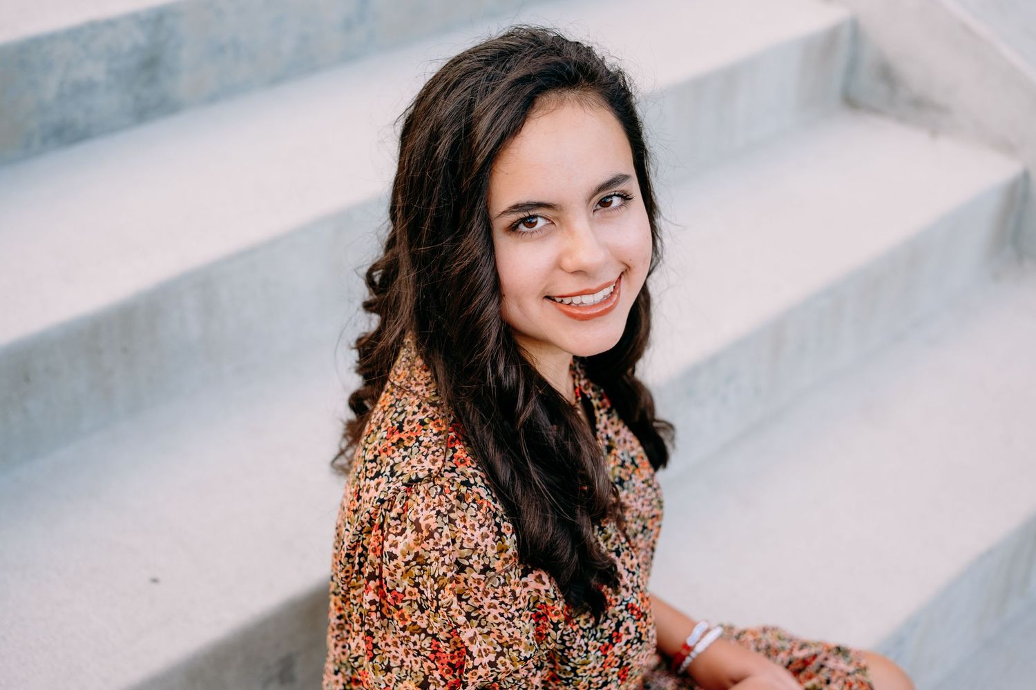 Senior portrait of teen sitting on cement stairs, smiling up toward camera, in Golden Colorado.