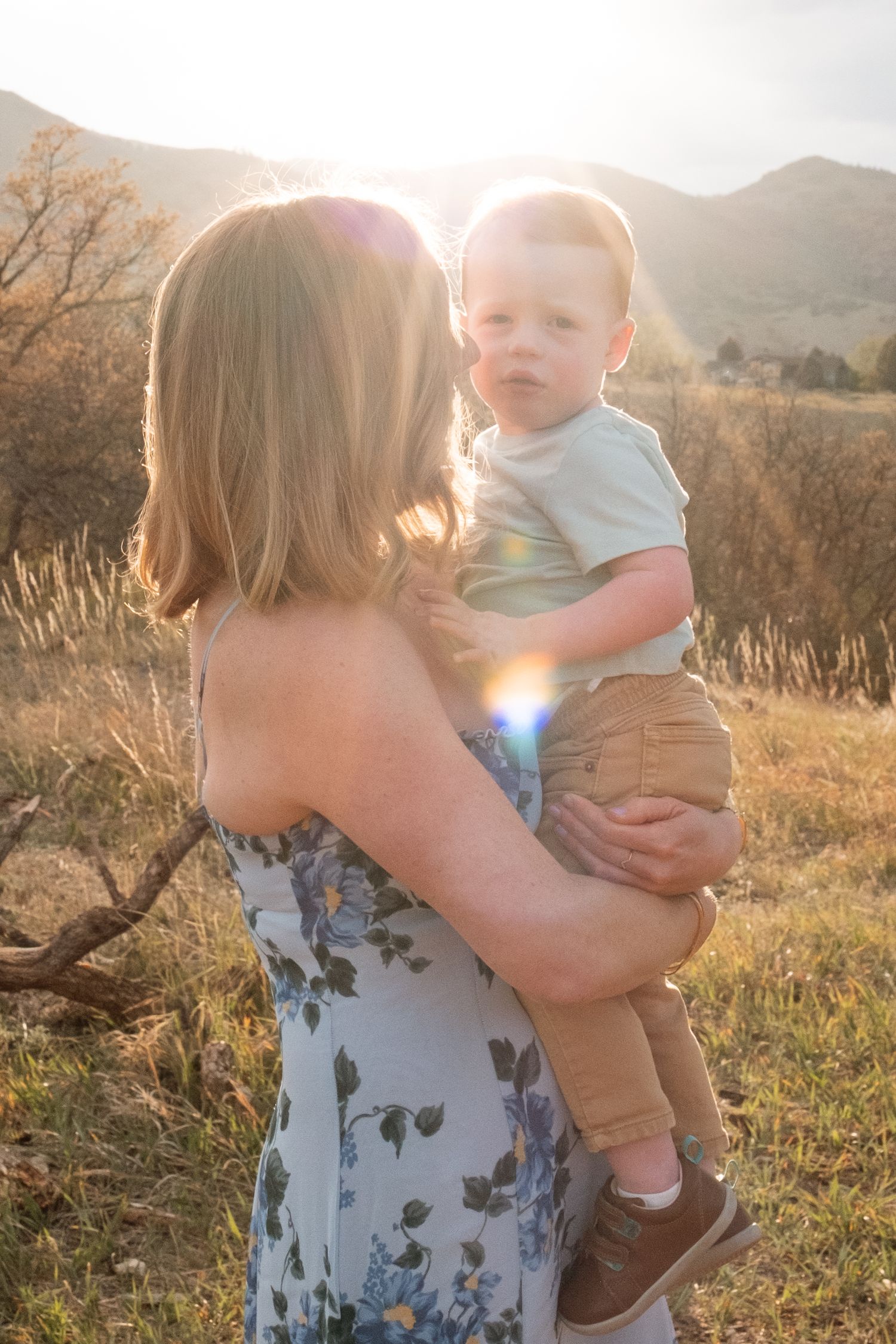 Mother holding son, back lit by the sun and foothills.