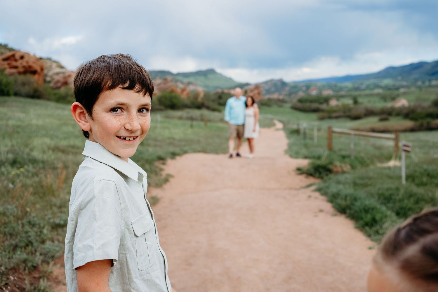 Boy looking mischievously toward camera, mother and father standing in background.