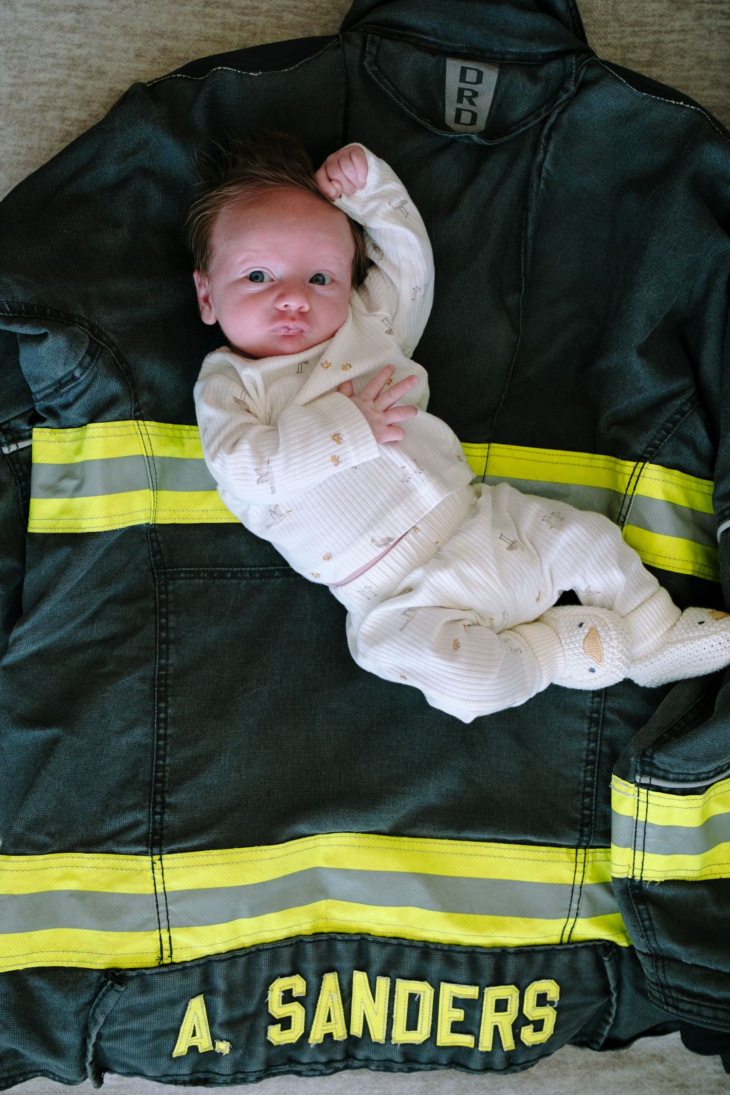 Newborn baby laying on mom's firefighter jacket.