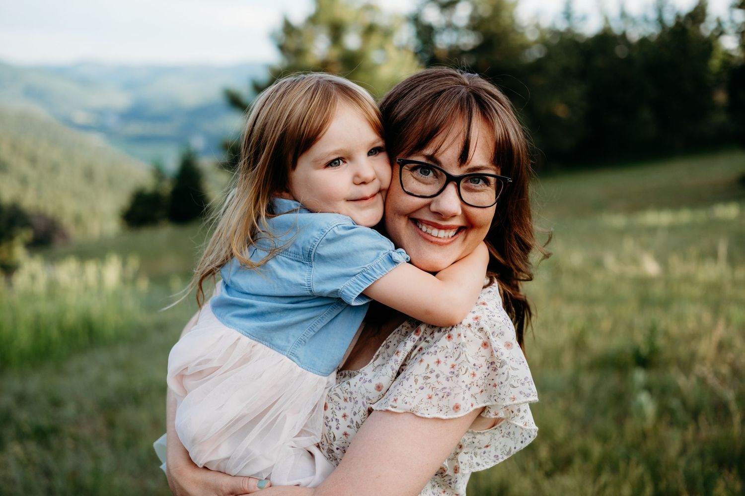 Mother holding young daughter, cheek to cheek, both with wide smiles.