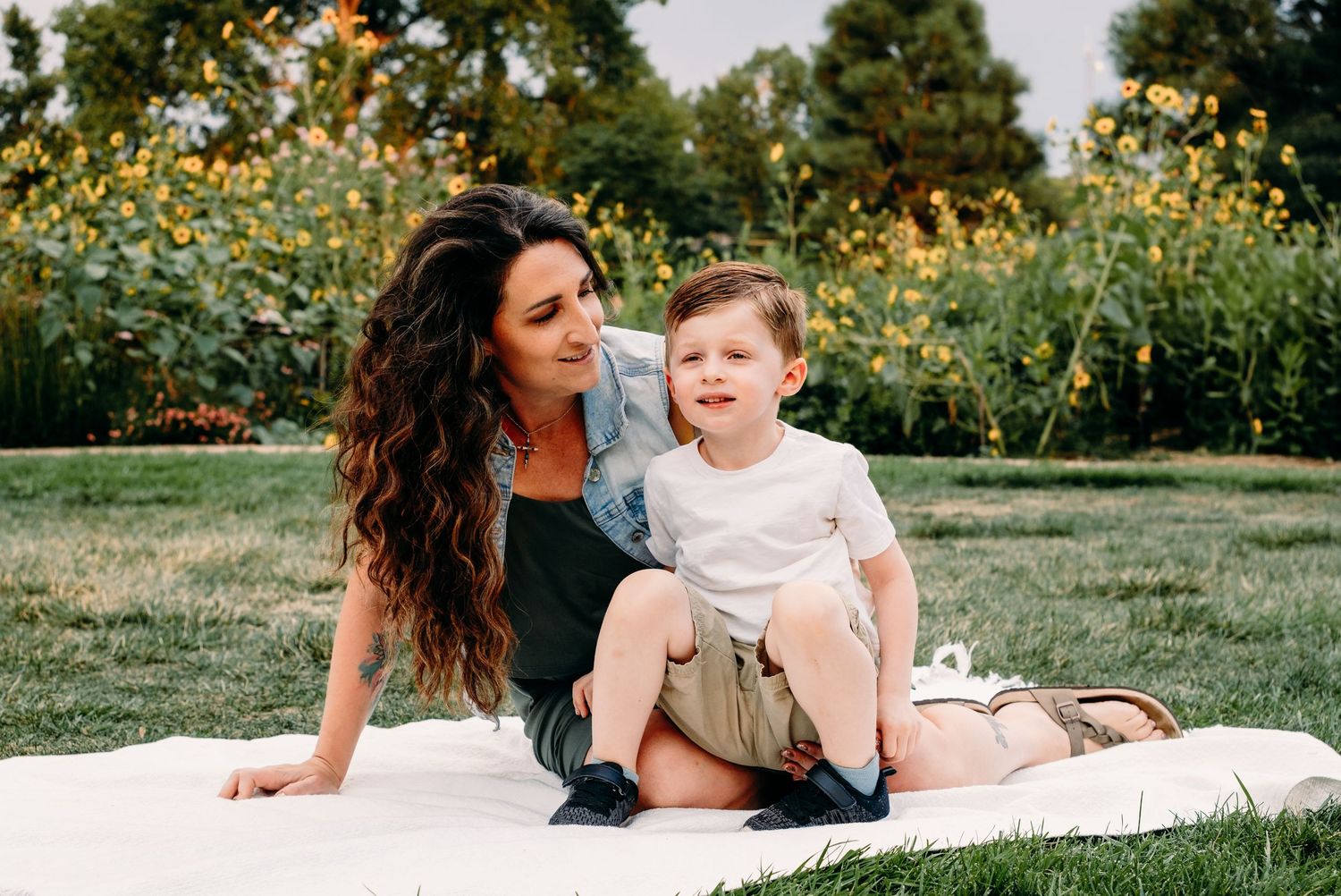 Mother and son sitting on grass, mother peering and smiling at son.