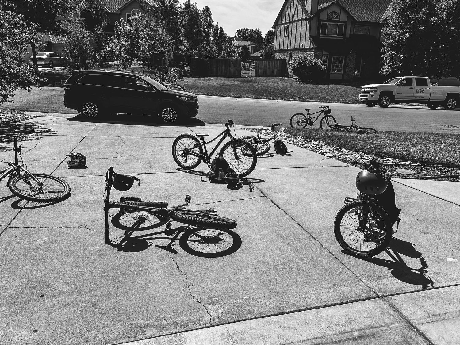 Black and white portrait of children's bikes askew on driveway.