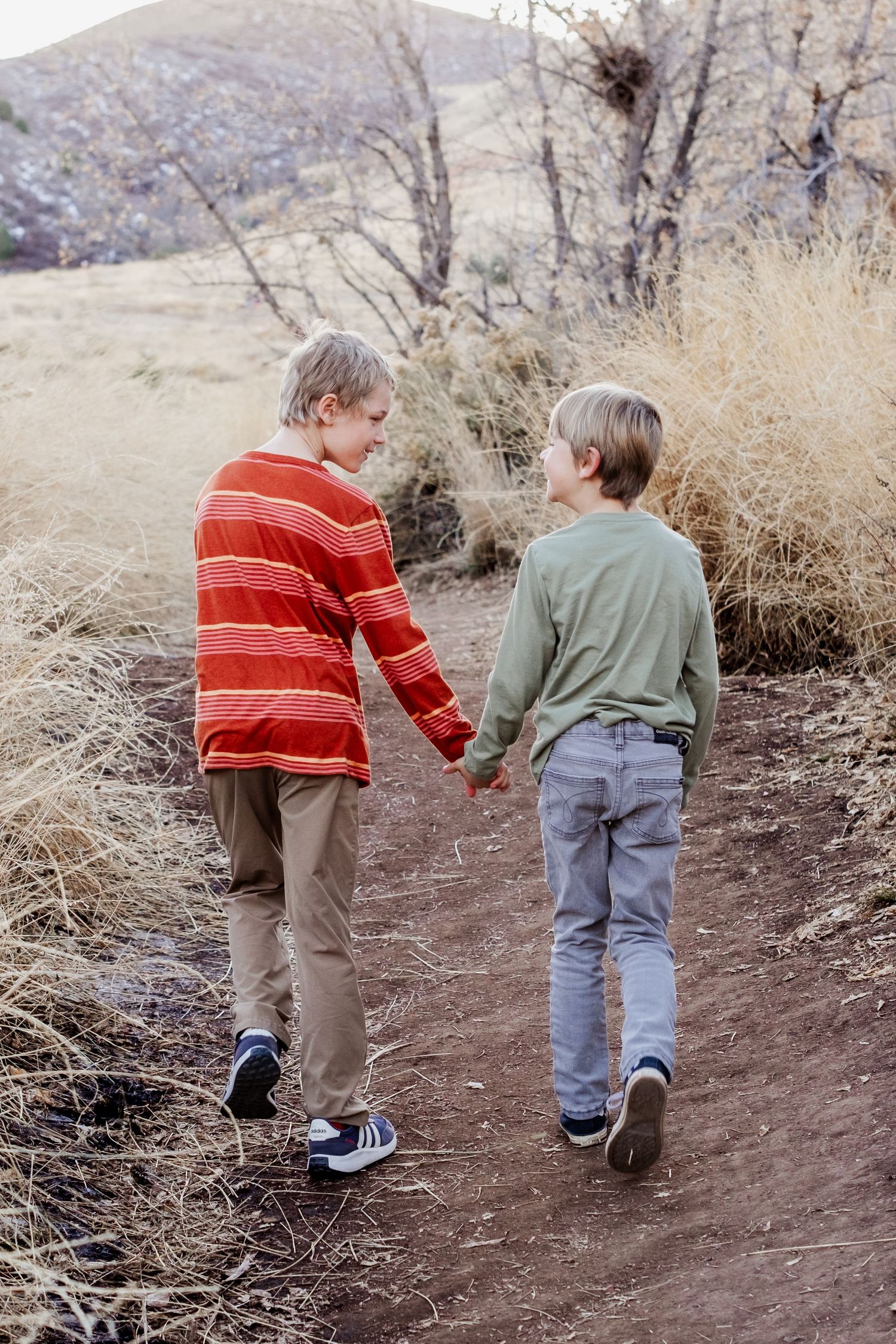 Brothers walking along dirt trail, holding hands, walking toward foothills.