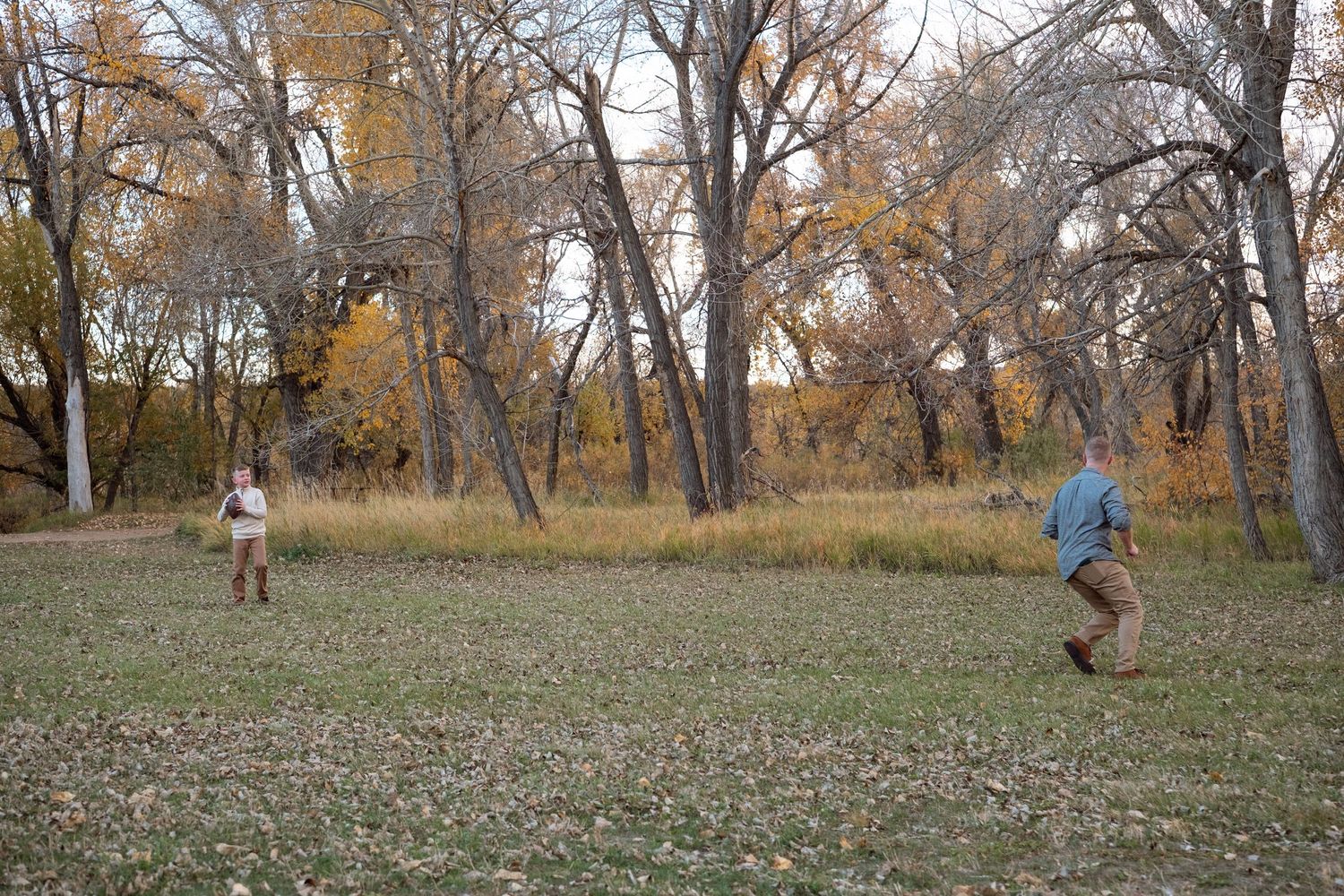 Father and son playing catch with a football in an open field at  Bear Creek Lake in Lakewood, Colorado.