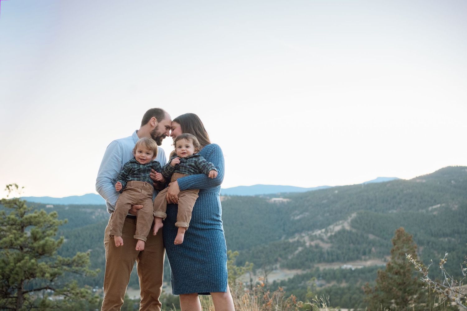 Mother and father, each holding a twin, pressing foreheads together, stunning mountain scene in the background at Mt Falcon West.