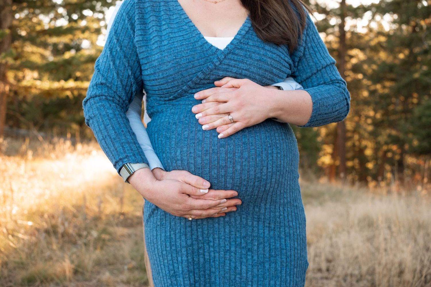 Close up of maternity portrait of mother, father standing behind her, both holding the top and bottom of her belly.