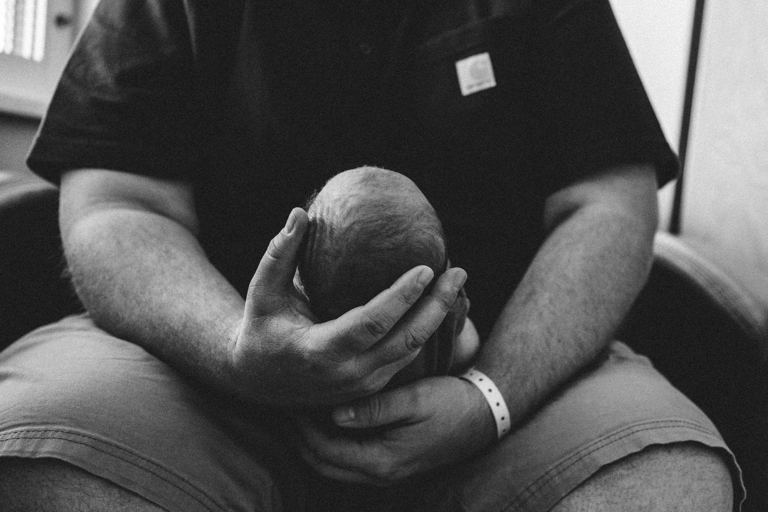 Father holding newborn baby, carefully holding newborn's tiny head in his palms.