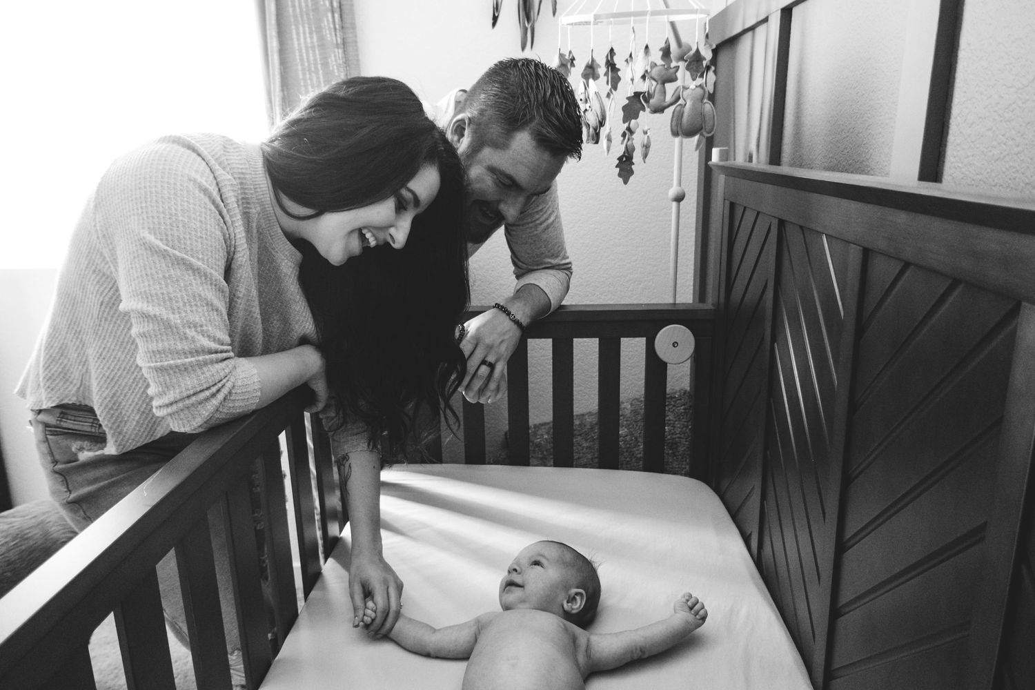 Mother and father reaching into crib to hold the hands of newborn baby boy.