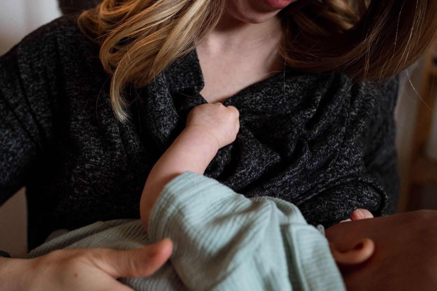 Mother feeding newborn, newborn holding onto mother's shirt.