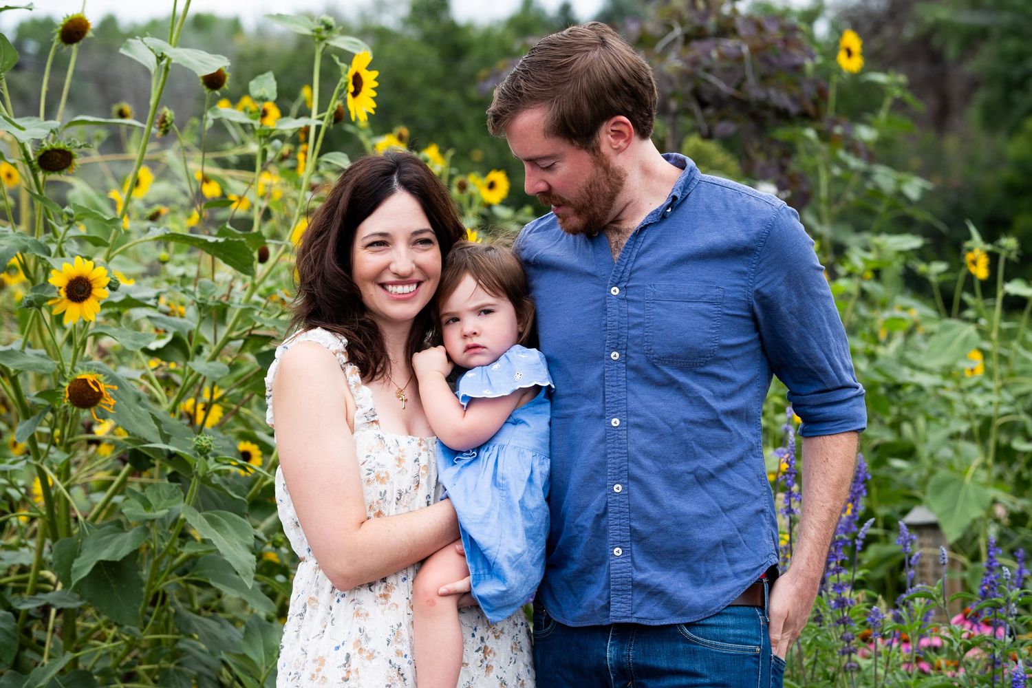 Mother, father and toddler daughter standing in sunflower garden.