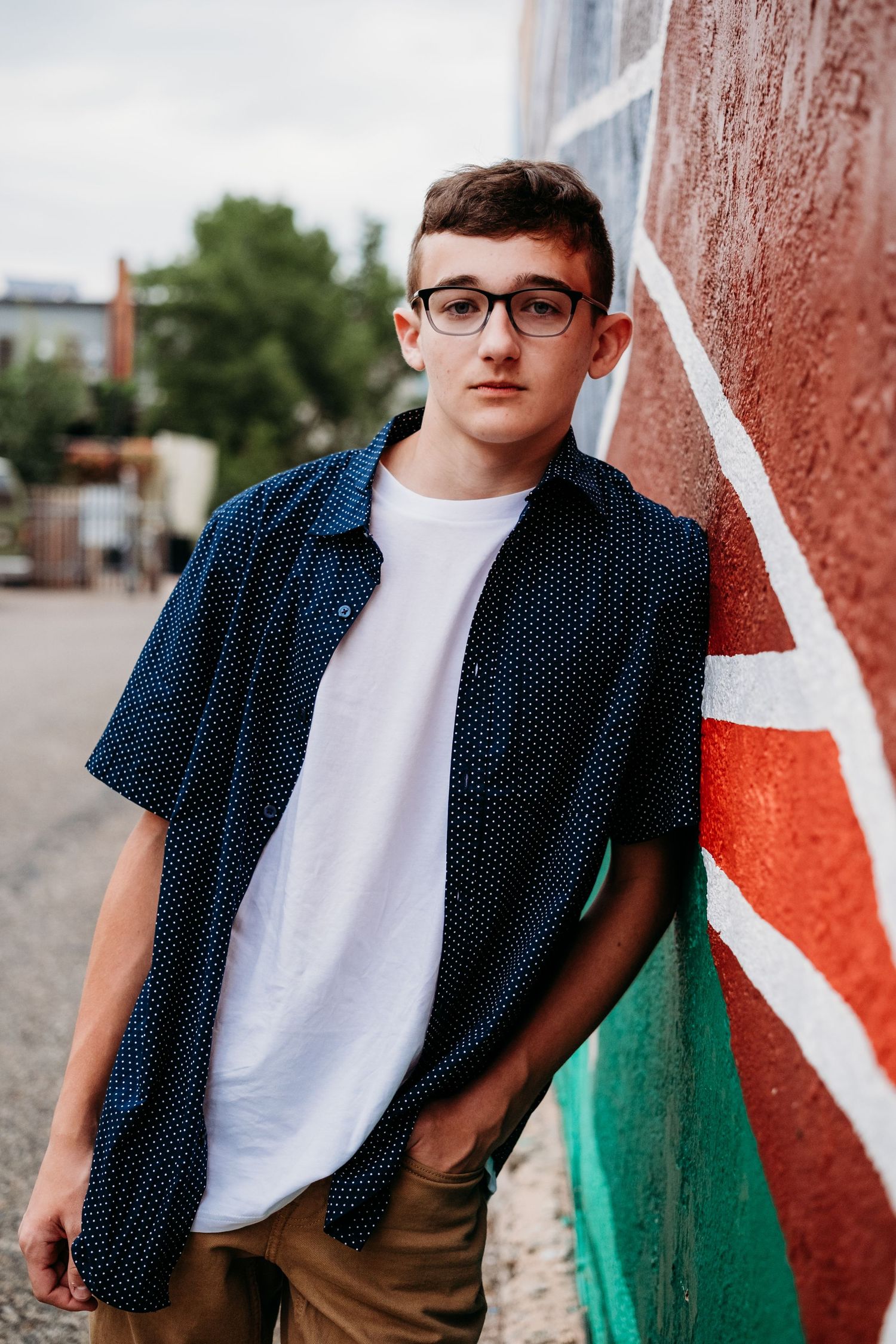 Senior portrait of a teen boy leaning against colorful mural in downtown Fort Collins,