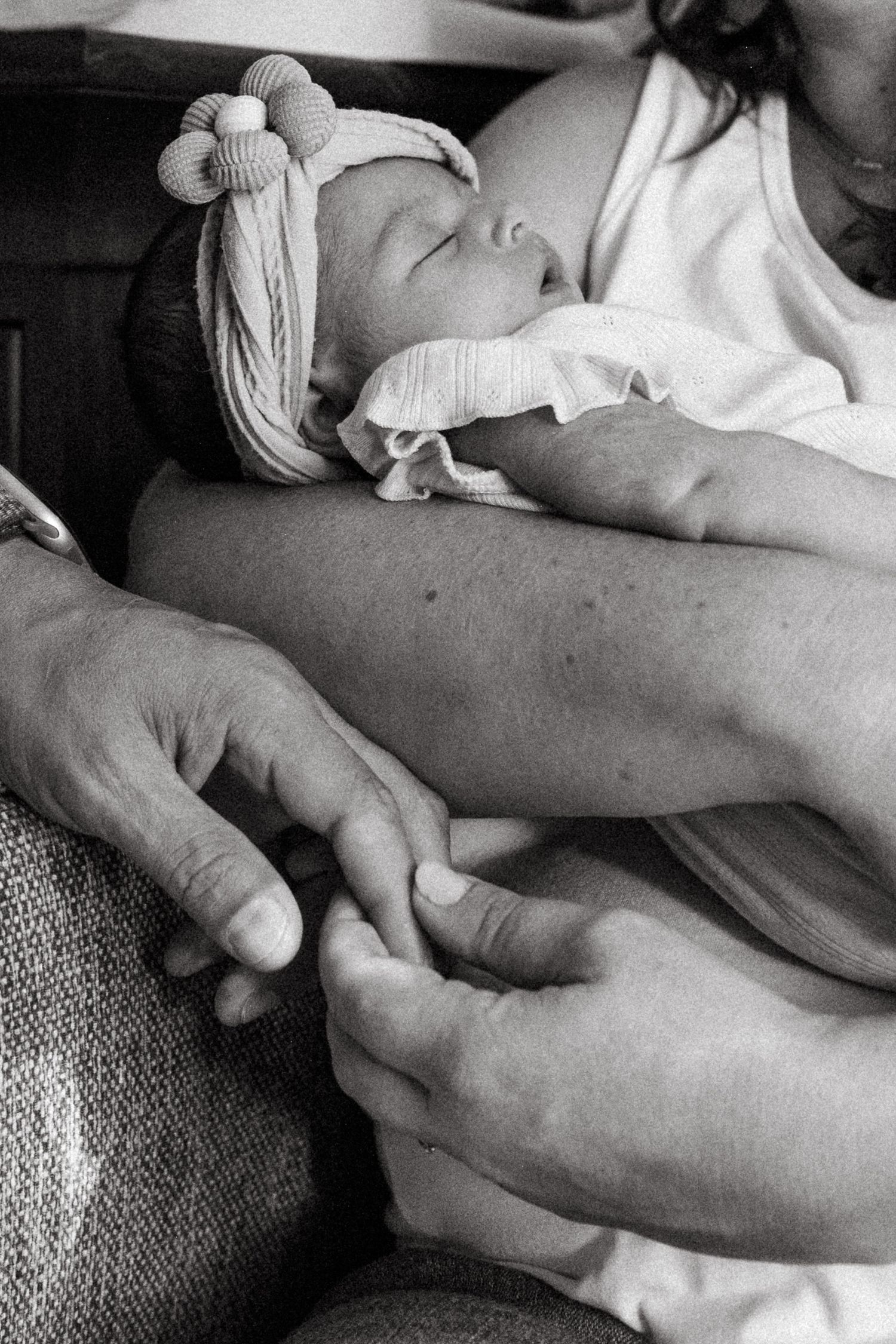 Black and white close up of mother holding newborn in her arm, father holding her other hand.