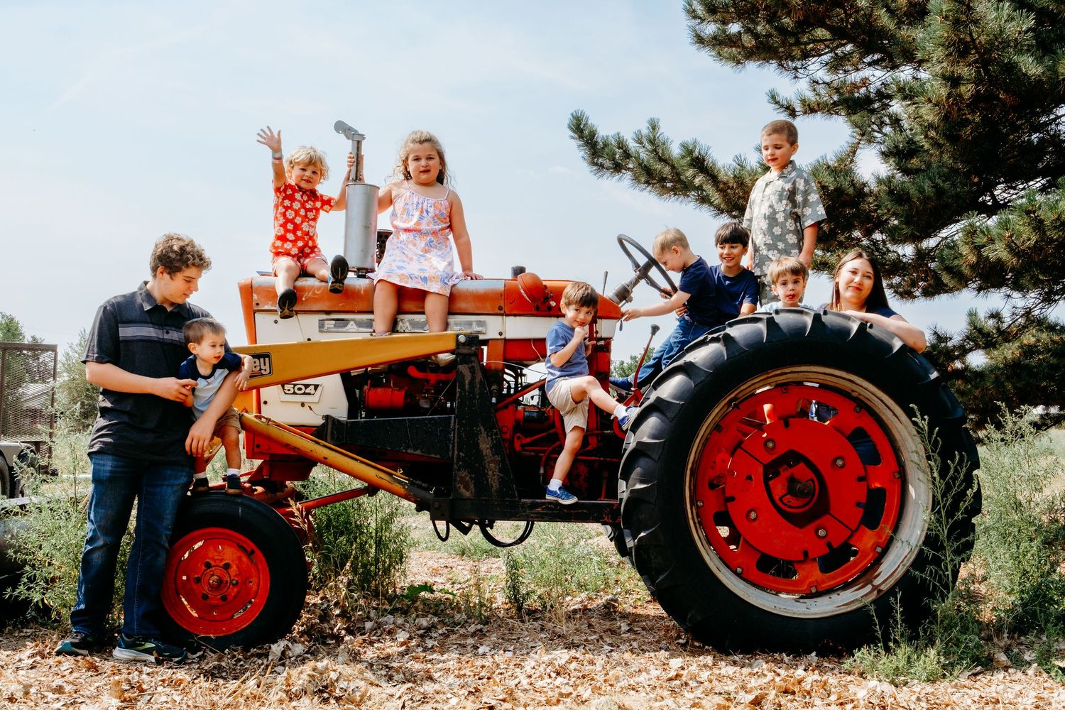 Cousins of various ages perched on a red tractor at family farm.
