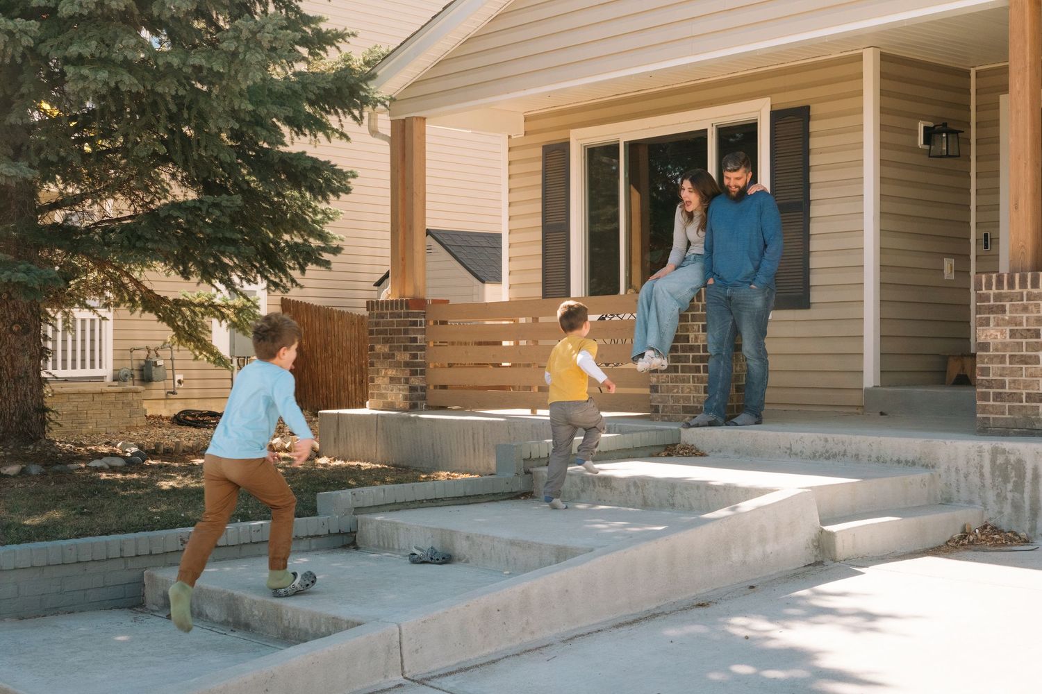 Boys running playfully up the front stairs to their parents who are sitting on their front porch.