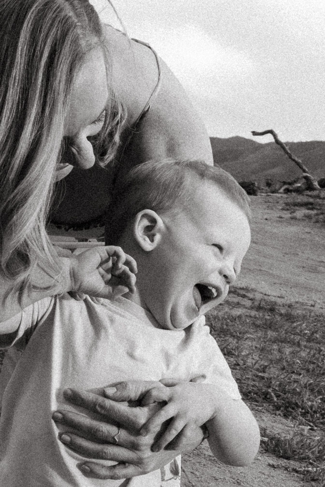 Black and white of mother chasing toddler, toddler laughing out loud.